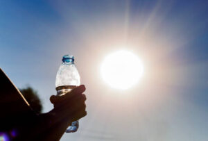 bottle-with-water-in-a-womans-hand-against-bright-sun-outdoors-climate-change-hotness-concept
